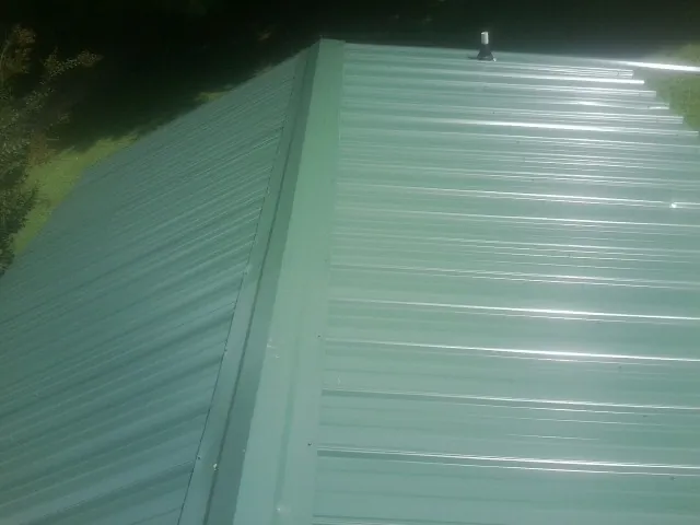 New green metal panels meeting at the ridge of a roof — Flat Roof Repair work by our crew in Fort Pierce