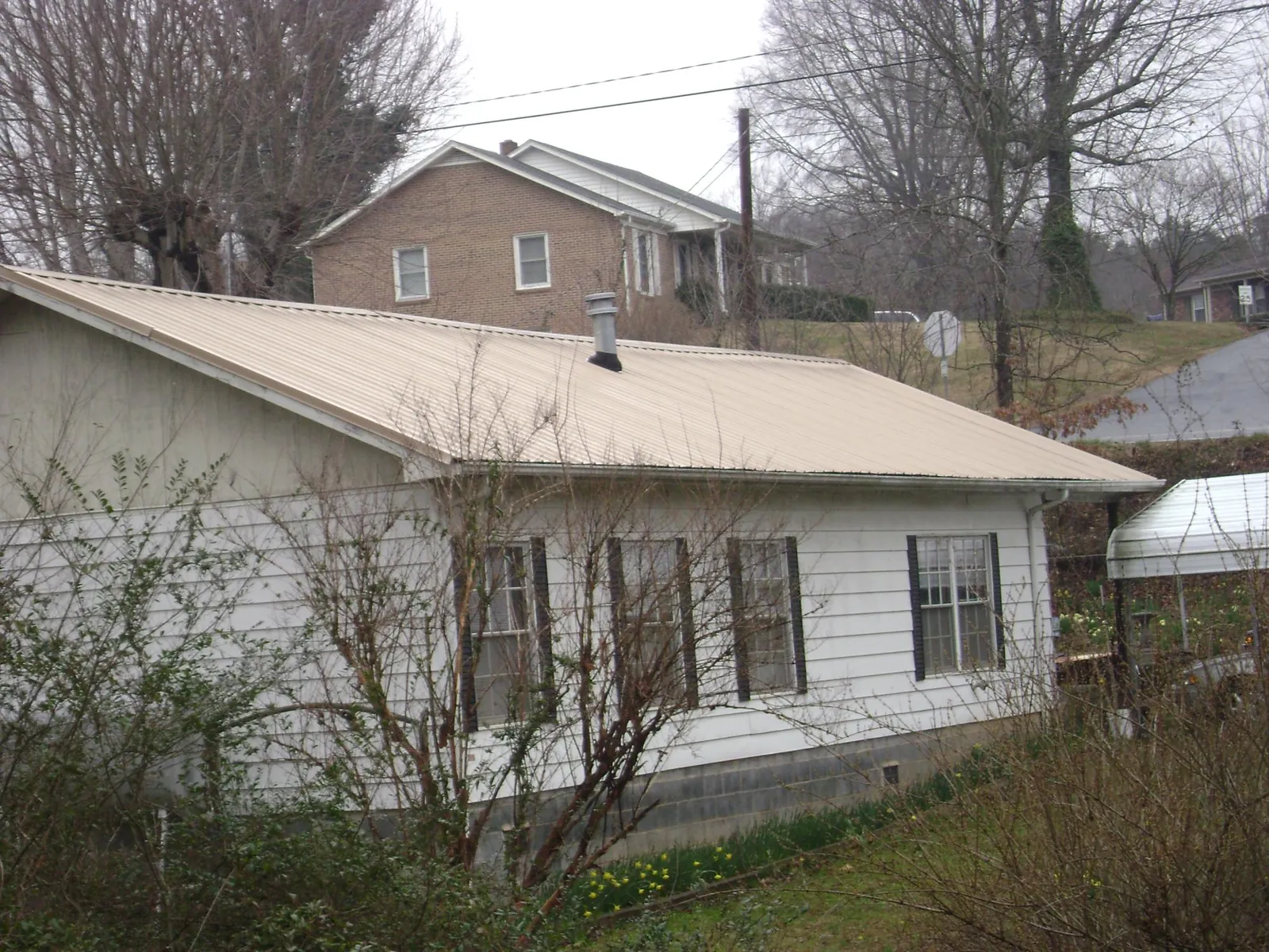 Tan metal roof on a white sided house set into a hillside — Commercial Roofing by Roofing Brothers in Fort Pierce