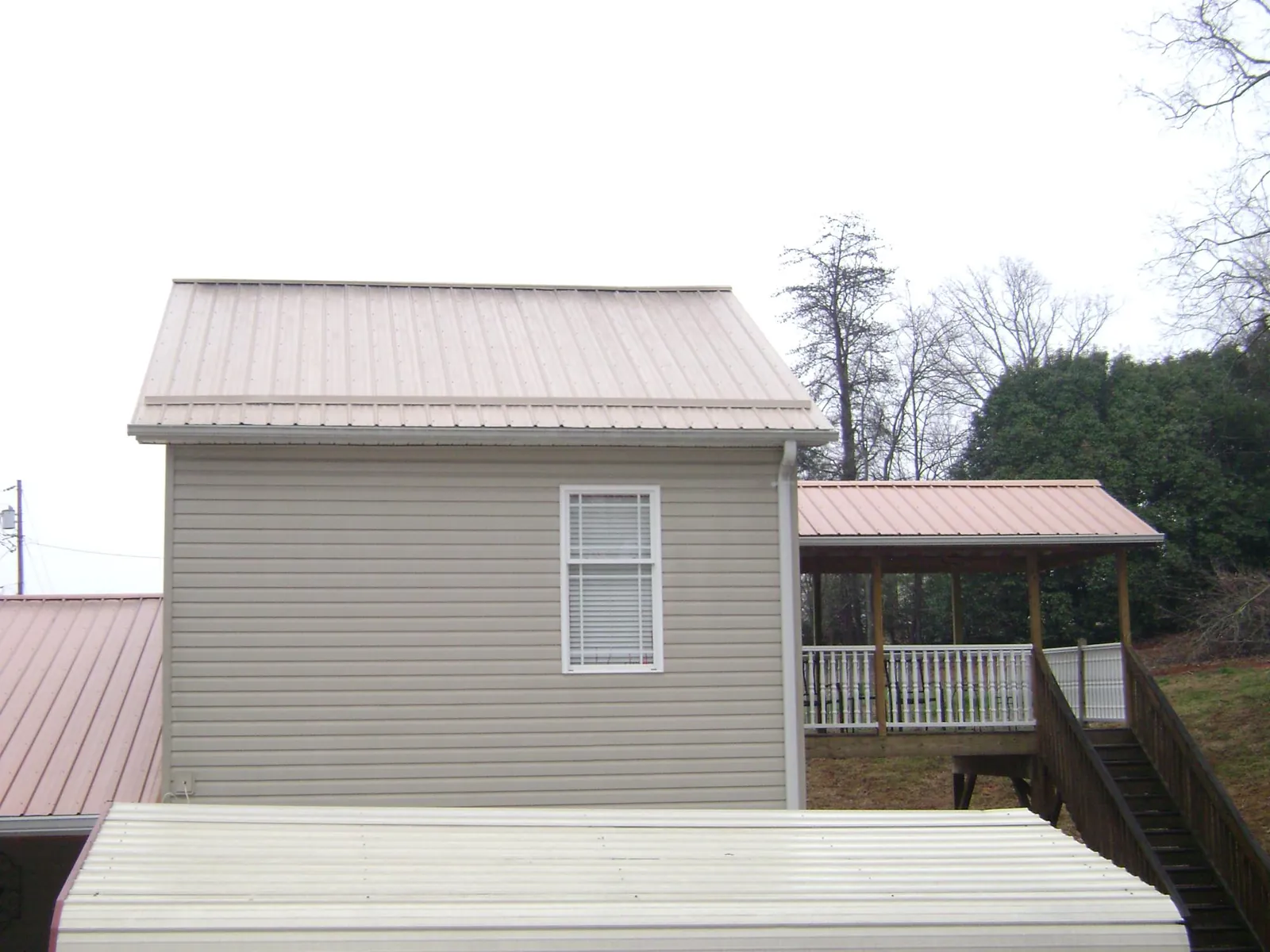 Tan metal roofs on a two story addition and attached porch, from a Roof Replacement job in Fort Pierce